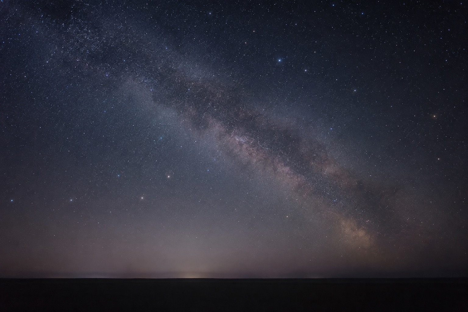 A clear night sky over a flat dark horizon, long exposure