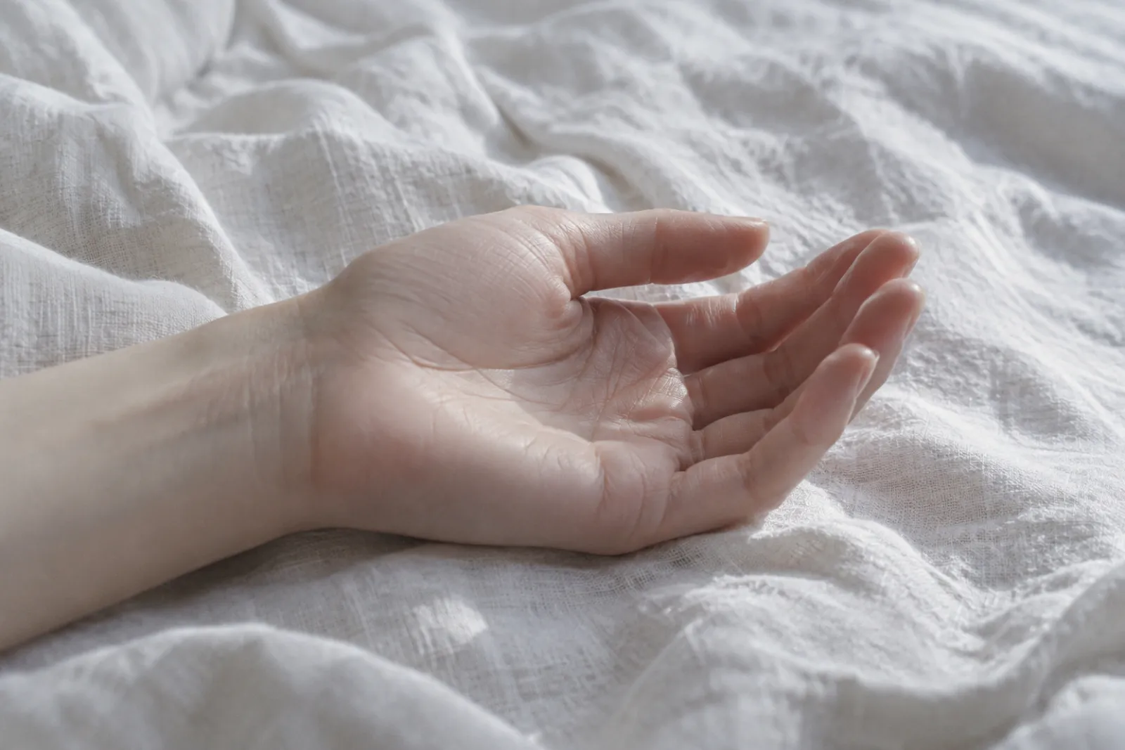 A hand palm up on a pale linen sheet, close crop, silver daylight