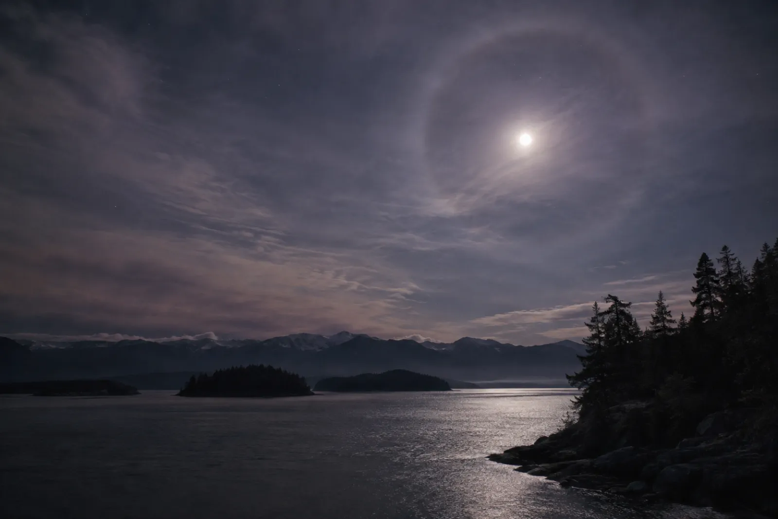 A faint halo around the moon through thin high cloud, night sky