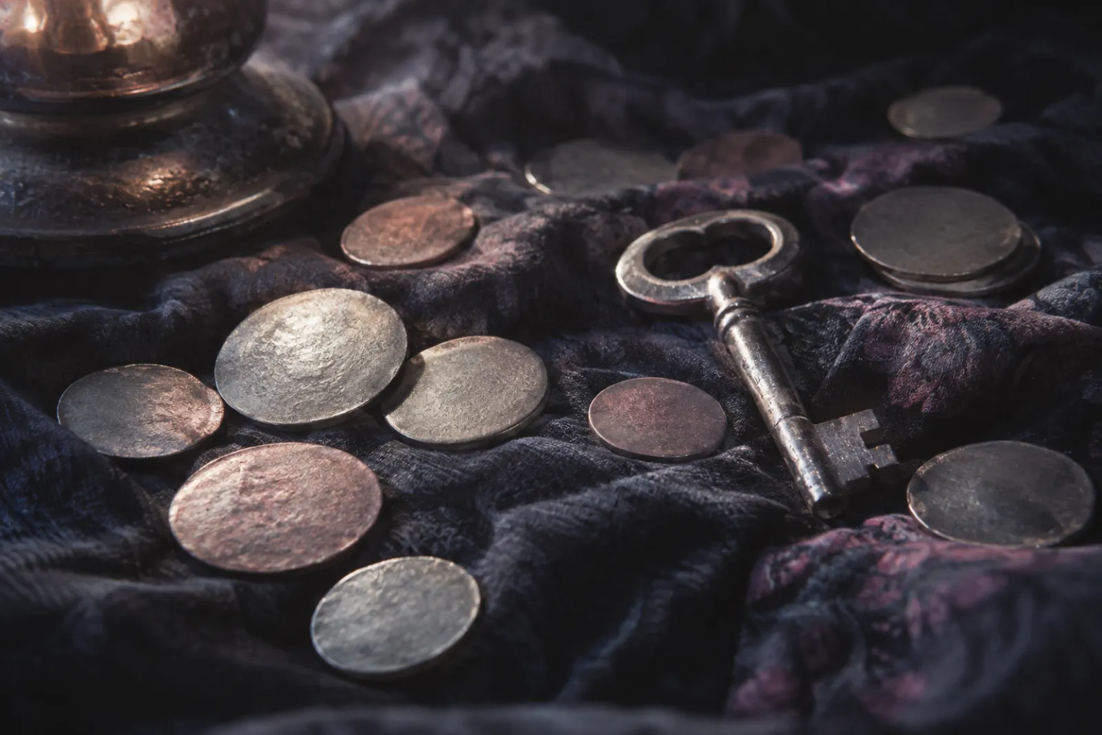 Coins and a lost key on dark cloth, one low source, silver highlights
