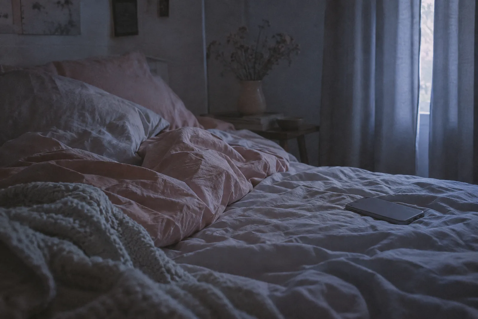 An unmade bed at three in the morning, grey-blue light through a gap in the curtains, a phone face down on the sheet