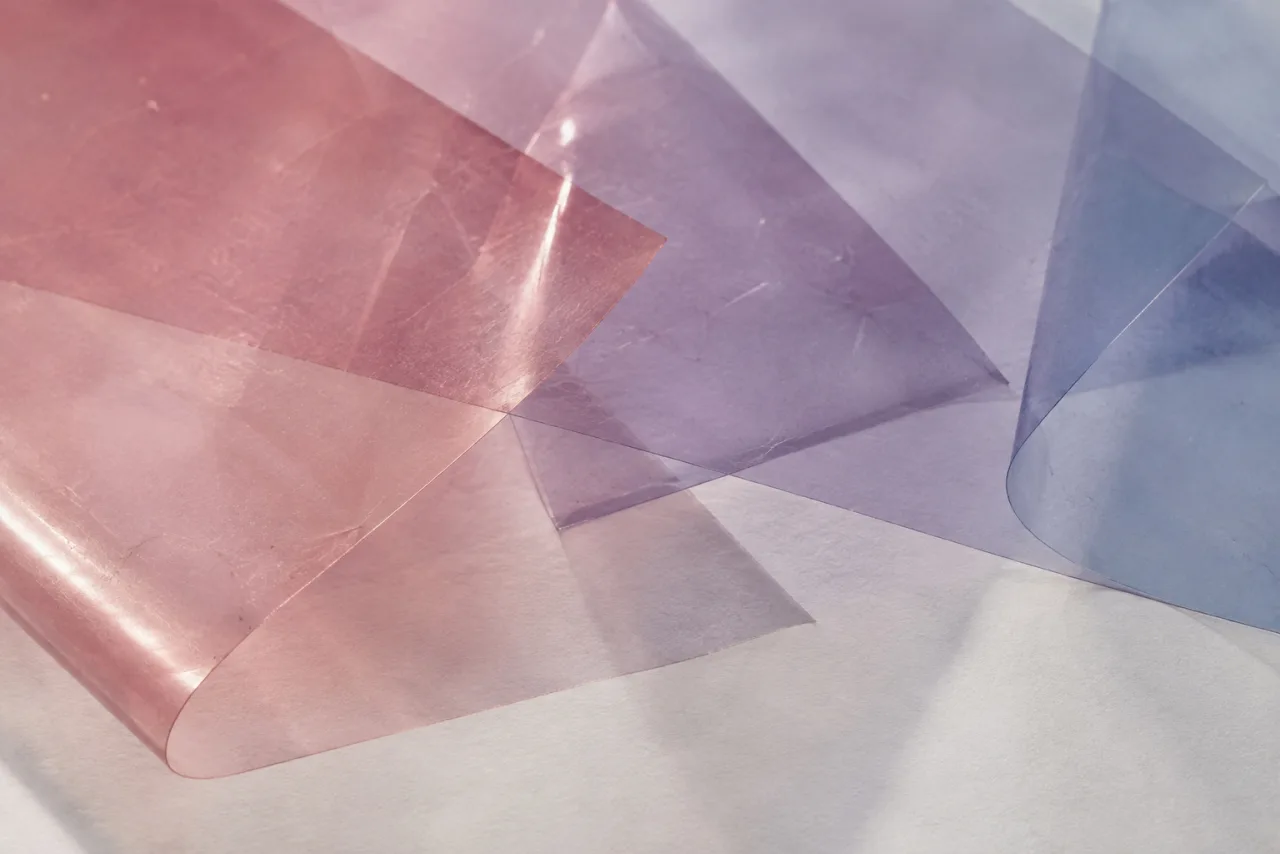 Layered translucent sheets on white paper, pink through lavender to blue, studio light