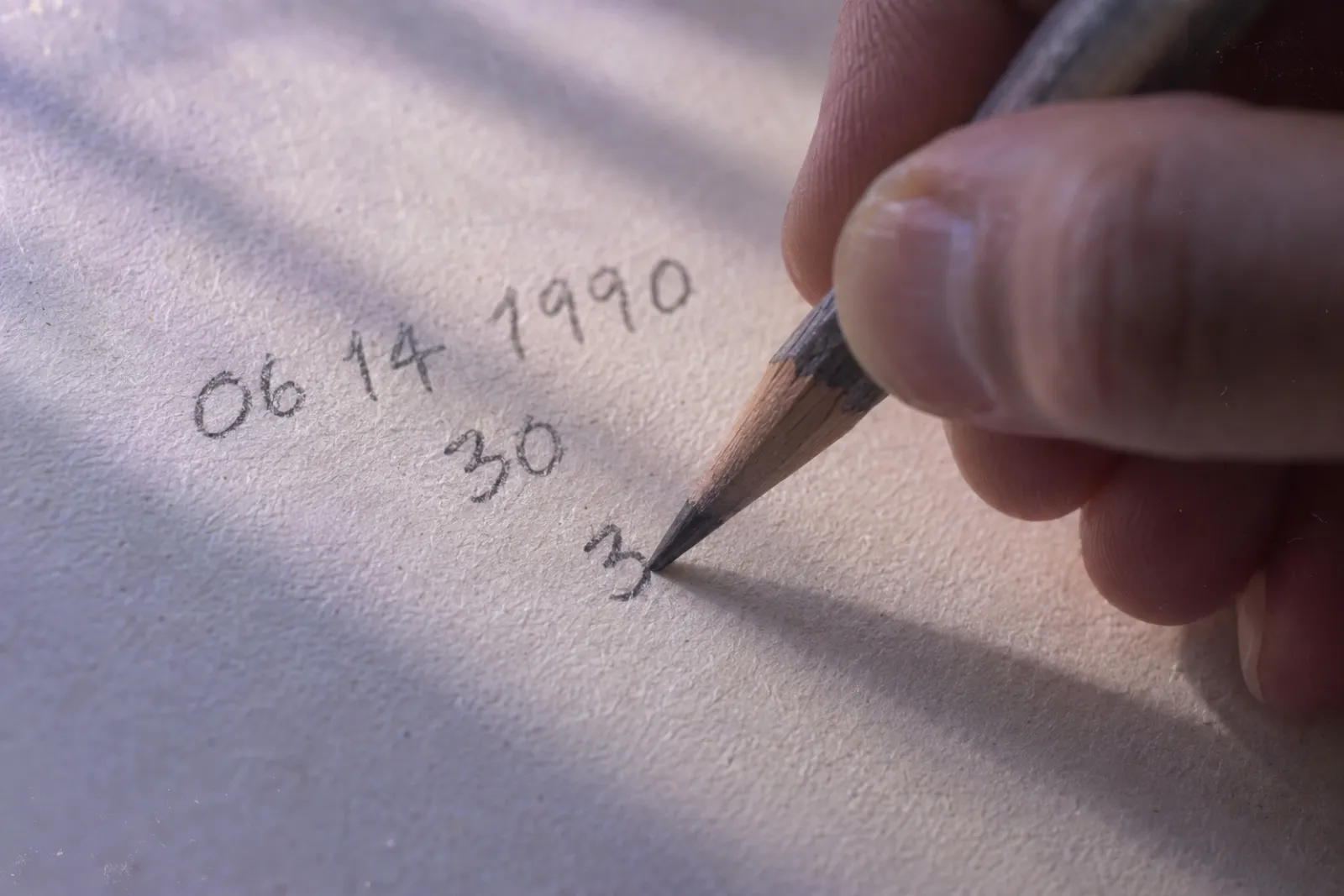 Close up of a hand writing a birth date down a sheet of cream paper in pencil