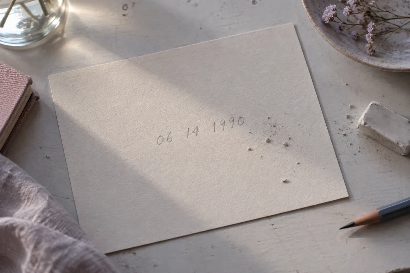 A birth date written in pencil on cream board seen from above, eraser crumbs beside it